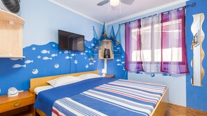 Un dormitorio con cama, televisor, mesita de noche y estante con adornos.