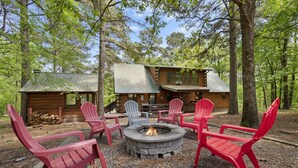 A cabin with a fire pit and red Adirondack chairs in a wooded area. - Family Friendly Luxury Log Cabin (Broken Bow)