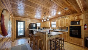 A wooden cabin kitchen with a central island, bar stools, wooden cabinets, a microwave, and a refrigerator. - Family Friendly Luxury Log Cabin (Broken Bow)