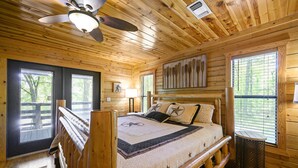 A wooden cabin bedroom with a bed, a ceiling fan, and a window with blinds. - Family Friendly Luxury Log Cabin (Broken Bow)