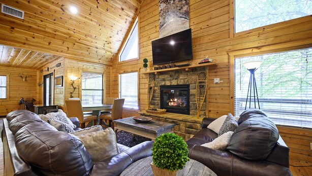 A cozy cabin interior with a leather sofa set, a stone fireplace, and a television mounted on the wall. - Family Friendly Luxury Log Cabin (Broken Bow)