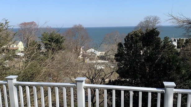 Une terrasse dotée d’une balustrade blanche, qui offre une vue sur une zone côtière avec des bâtiments et des arbres.