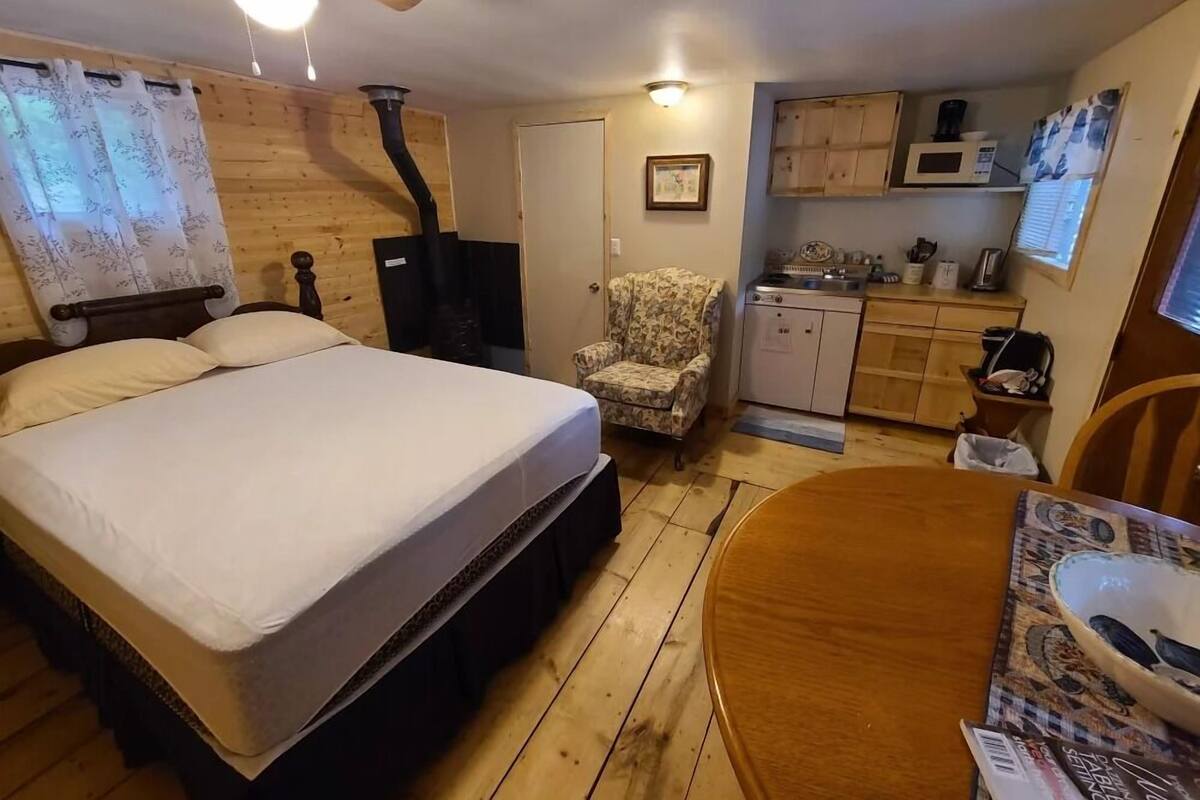 A compact room with a bed, a chair, a small table, a microwave, and a sink.