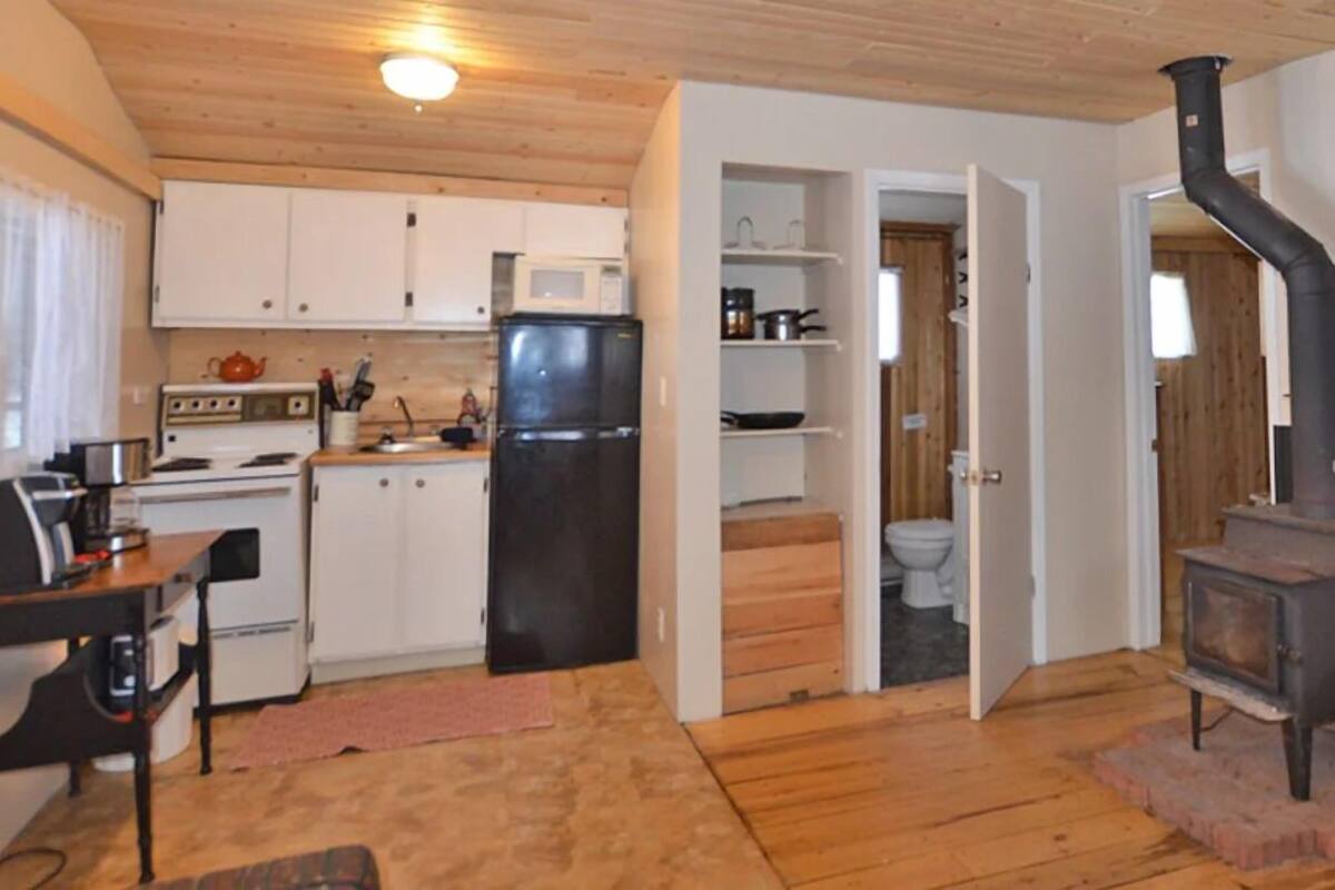 A compact kitchen with white cabinets, a black refrigerator, a stove, and a wood-burning stove.