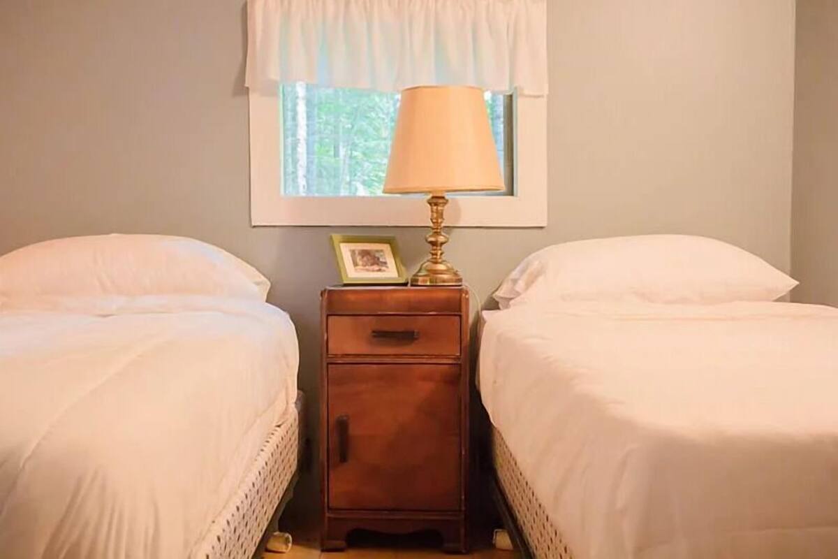 A bedroom with two single beds, a nightstand with a lamp, and a window with a curtain.