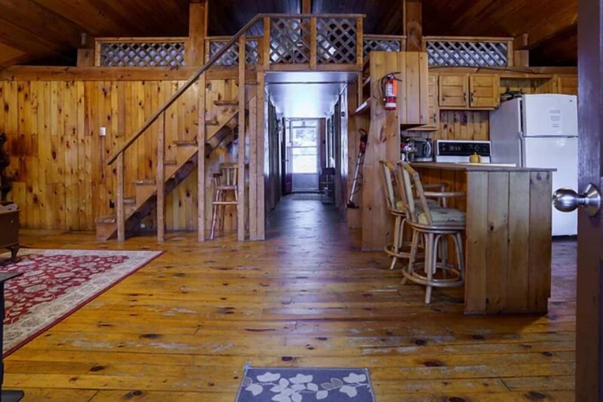 A rustic wooden interior with a kitchen area, wooden staircase, and a dining area with chairs.