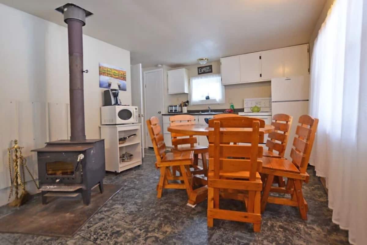 A compact kitchen with white cabinets, a stove, and a dining area with wooden chairs.