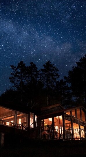 A building with a starry night sky view, wooden exterior, and illuminated windows. - Mattawa River Resort (Papineau-Cameron)