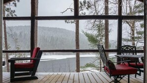 En træterrasse med to røde stole og et bord, med udsigt over et snelandskab gennem store vinduer.