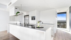 A modern kitchen with white cabinetry, a central island, and a view of the city. - Circle on Cavill Ocean View  Surfers Paradise (Surfers Paradise)
