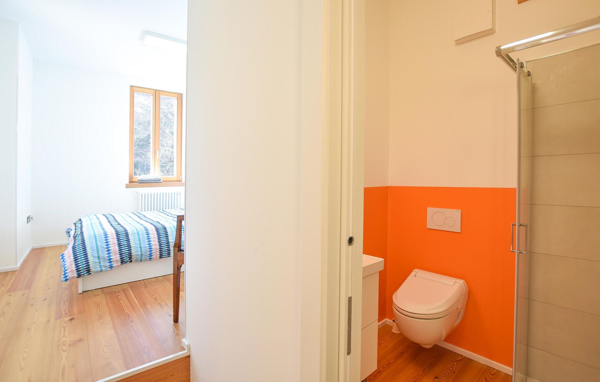 A room with a bed, a white toilet, and a window with a view of trees.