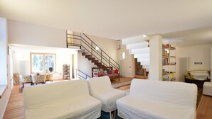Een ruime woonkamer met een trap, witte meubels en een boekenkast.