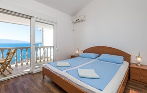 Une chambre à coucher avec un lit en bois, deux lampes de chevet, une table de nuit et une vue sur la mer, visible à travers une porte-fenêtre coulissante.