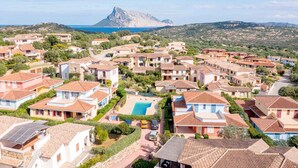 Una zona residenziale costiera con case, una piscina e una montagna imponente sullo sfondo.