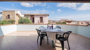 Portico esterno coperto con un tavolo rotondo apparecchiato per mangiare, circondato da sedie, con vista su una zona residenziale con edifici in pietra.