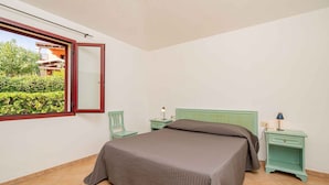 Una camera da letto con un letto, un comodino, una sedia e una finestra con porta aperta.