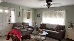Ein Wohnzimmer mit einem braunen Ledersofa, einem gemusterten Sessel, einem Couchtisch und einer weißen Kommode.