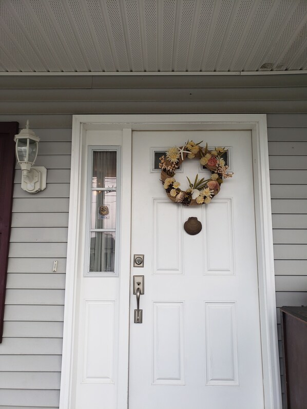 A white door with a decorative wreath, a small window, and a doorbell.