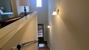 Un escalier en bois avec une rampe, une petite fenêtre en haut et un luminaire fixé au mur.