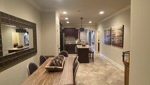 Une cuisine moderne avec des meubles de couleur sombre, un îlot central et un coin repas comprenant une table et des chaises en bois.