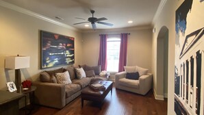 Un salon doté d’un parquet, d’un ventilateur de plafond, d’un grand tableau et d’une cheminée.