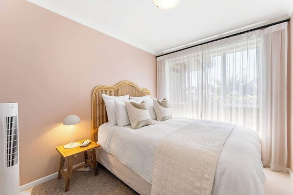 A neatly arranged bedroom with a bed, bedside table, lamp, and a window with sheer curtains. - Five Palms Luxury Beach Escape (Mount Maunganui)