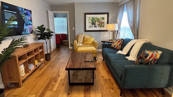 A living room with a wooden coffee table, a blue sofa, a yellow armchair, and a TV mounted on the wall. - Marjory's Cottage in the heart of Tampa (Tampa)