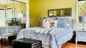 A bedroom with a bed, a ceiling fan, a nightstand, a mirror, and a window with a view of trees.