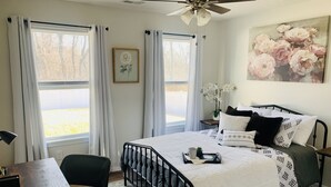 Une chambre à coucher comprenant un lit, un bureau, une chaise, une table de chevet et un ventilateur de plafond.