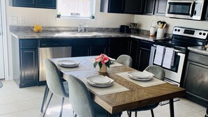 Une cuisine moderne avec des meubles de couleur sombre, un four à micro-ondes encastré et un coin repas comprenant une table et des chaises en bois.