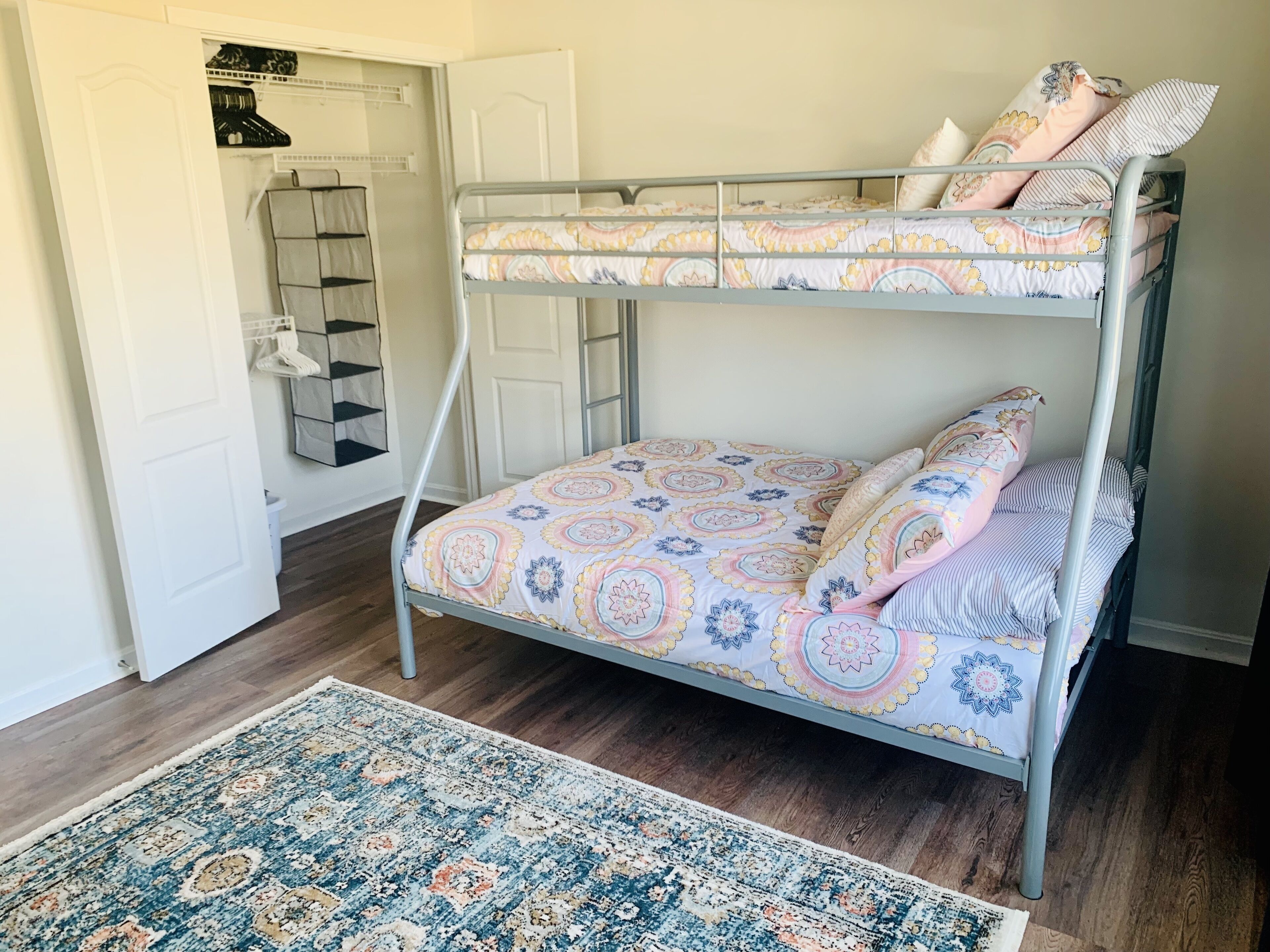 Een stapelbed met behang, een bergkast en een vloerkleed, alles in een kamer met houten vloeren.