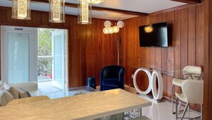 A modern living room with a wooden wall, a flat-screen TV, a glass coffee table, and a blue chair. - New*Quiet Nature view #3; 1/1, pool, walk to beach (Fort Myers Beach)