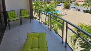 Un balcón con sillas acolchadas verdes, una piscina y vistas a un complejo de edificios.