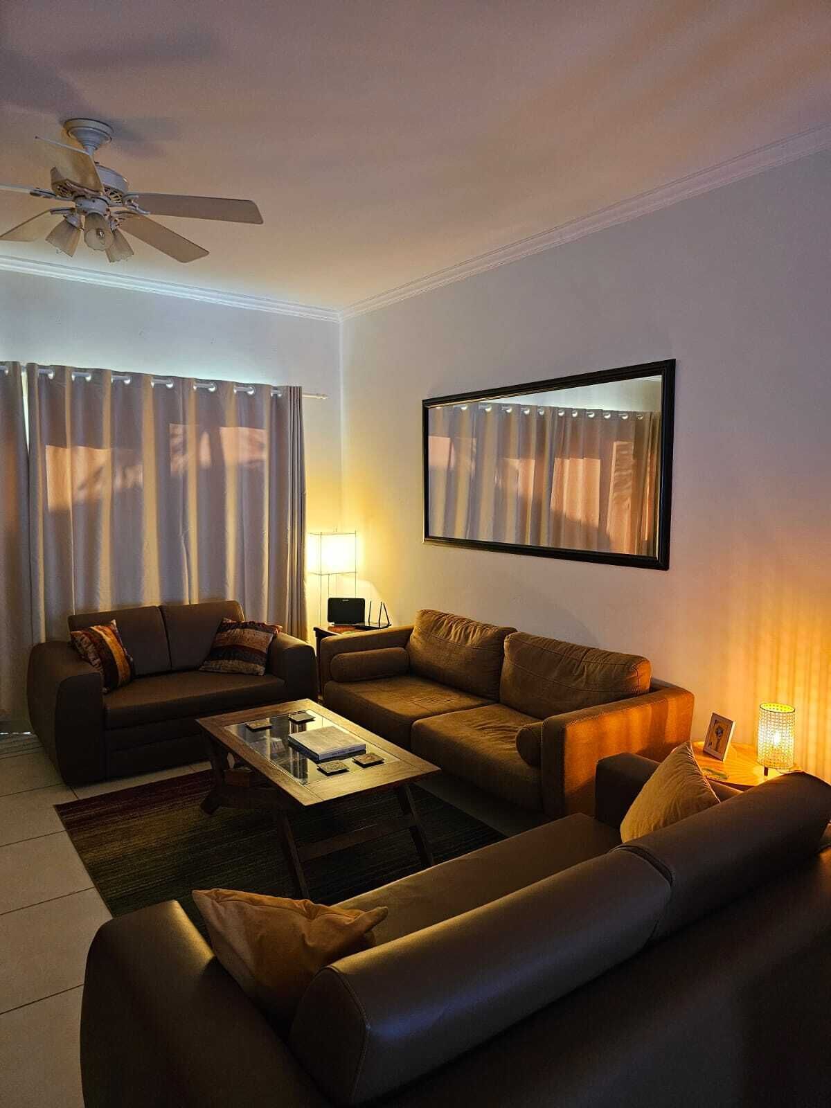 Un salon avec un ventilateur de plafond, deux canapés, une table basse et un téléviseur posé sur un meuble.