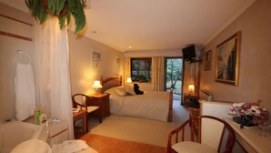 Habitación de hotel con cama, escritorio, silla, ventana con vistas a zonas verdes y un cuadro en la pared.