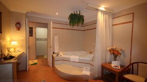 Habitación de hotel con bañera, lavamanos, espejo, reloj y planta.