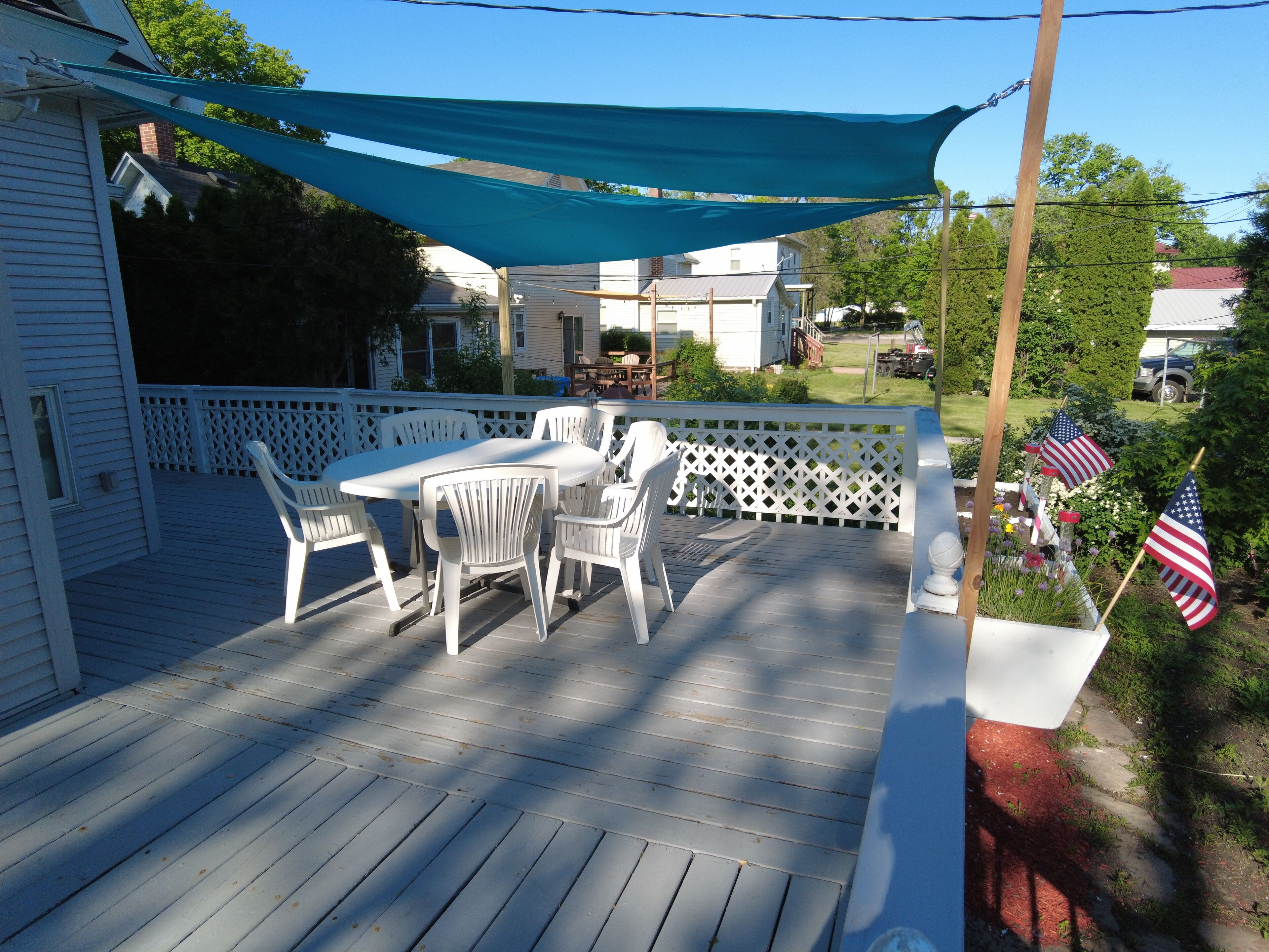 Une terrasse en bois avec une table et des chaises blanches, un auvent bleu et des drapeaux américains.
