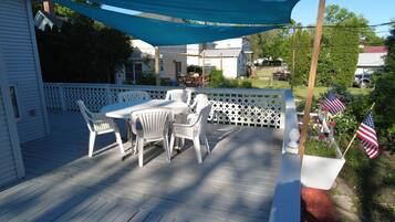 Une terrasse en bois avec une table et des chaises blanches, un auvent bleu et des drapeaux américains.