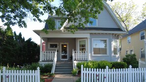 A two-story house with a front porch, a white picket fence, and a pathway leading to the entrance.