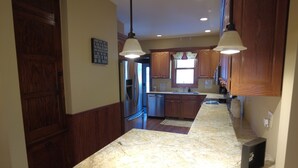 A kitchen with wooden cabinets, a stainless steel refrigerator, a built-in oven, a sink, and pendant lighting.
