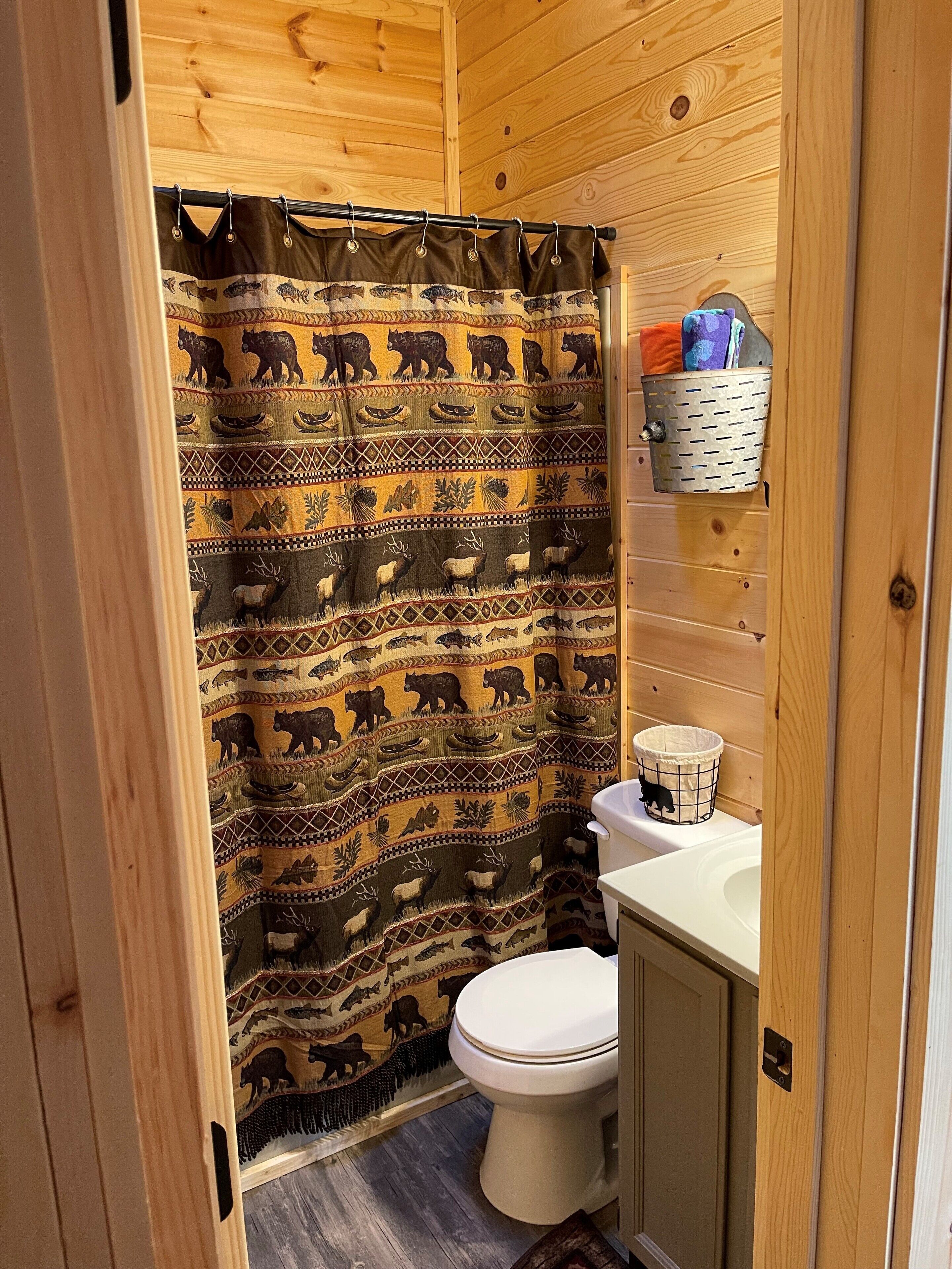 A bathroom with a wooden interior, a shower curtain with animal prints, a toilet, and a small shelf with toiletries.