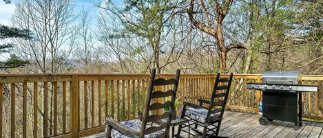 A wooden deck with two rocking chairs and a portable grill.