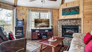 A cabin interior with a stone fireplace, a television on a wooden stand, a leather chair, and a couch with red cushions. - Gnoming Around (Gatlinburg)