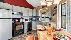 A modern kitchen with white cabinets, a wooden island, and a red accent wall. - Gnoming Around (Gatlinburg)