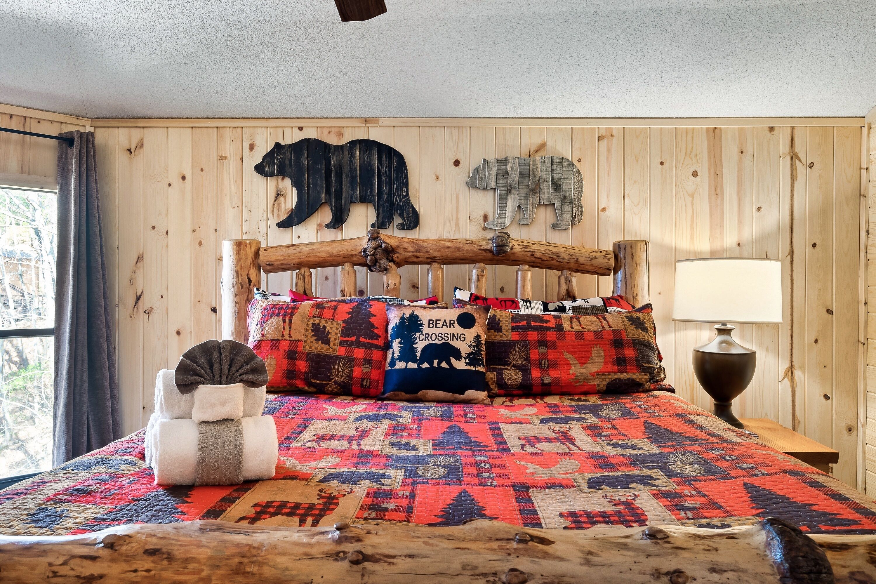 Ein Zimmer mit Holzwandverkleidung, einem Bett mit gesteppter Decke, Kissen mit Bärenmotiven und einem Holzbalken-Kopfteil.