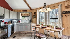 A kitchen with wooden cabinets, a dining table with stools, and a hanging light fixture. - Gnoming Around (Gatlinburg)