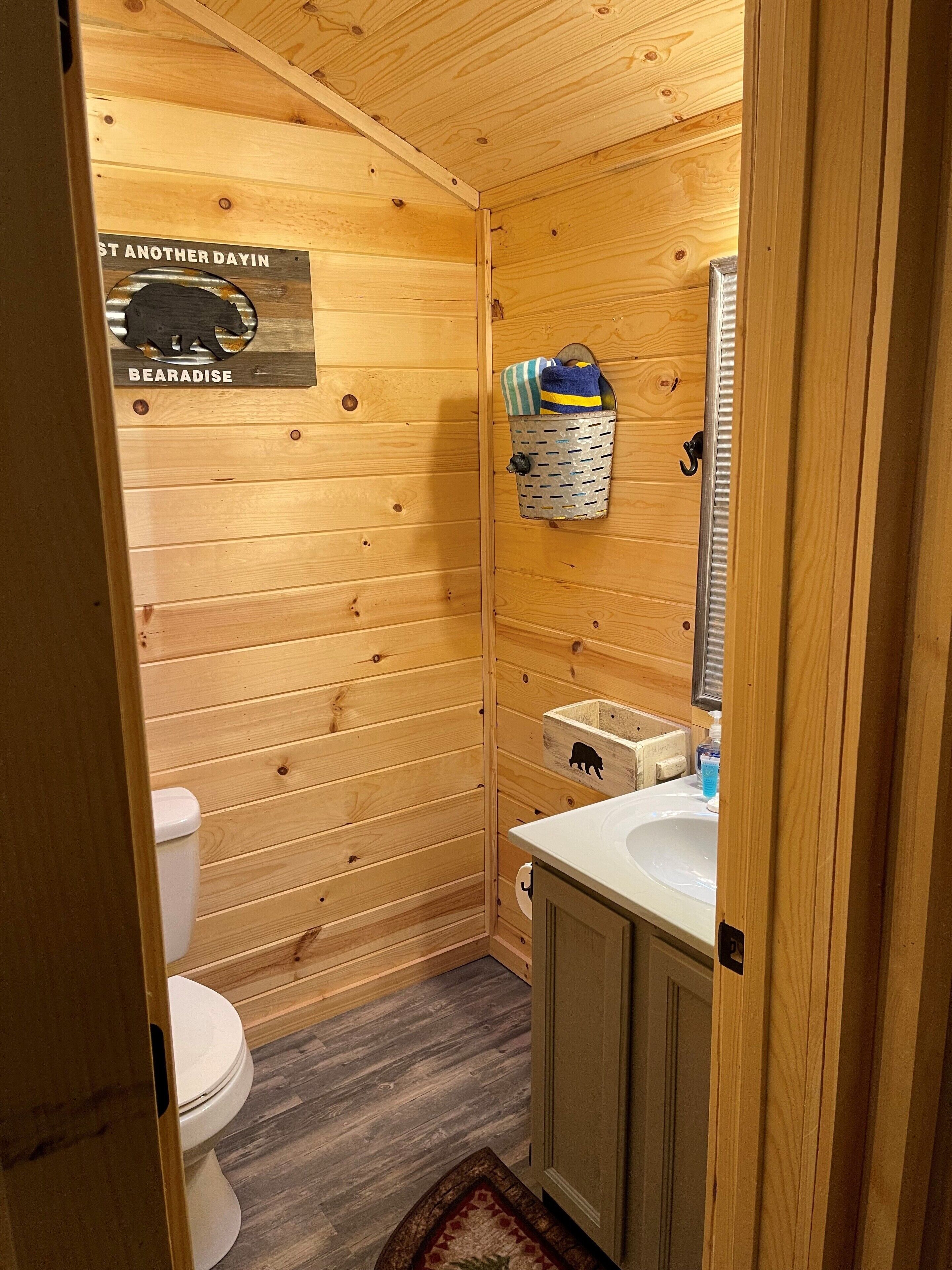 A wooden-paneled bathroom with a toilet, a sink, and a hanging laundry basket.