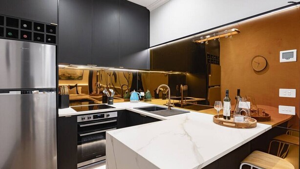 Une cuisine moderne dotée d’un grand îlot central, d’appareils électroménagers en acier inoxydable et d’un mur d’accent en bois.