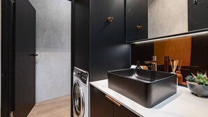 Une cuisine moderne dotée d’un lave-linge encastré, d’un évier noir et de meubles de rangement aux couleurs sombres.