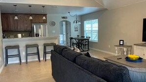 A modern kitchen with a central island, a dining area with a dark-colored sofa, and a ceiling fan.